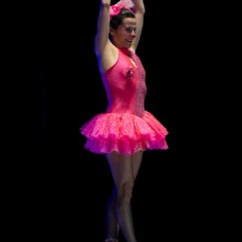 La bailarina de tutú rosado de espaldas, con un brazo en alto.