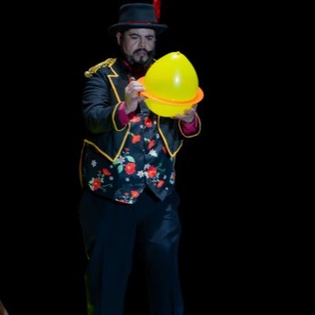Un payaso de chaqueta bordada sostiene un globo amarillo.
