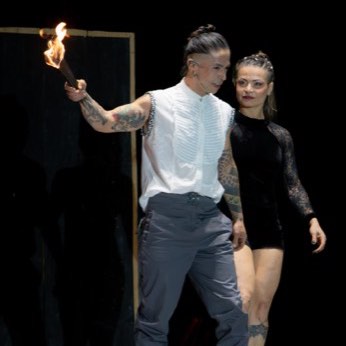Una pareja de artistas de pie en la pista, con antorchas encendidas detrás.