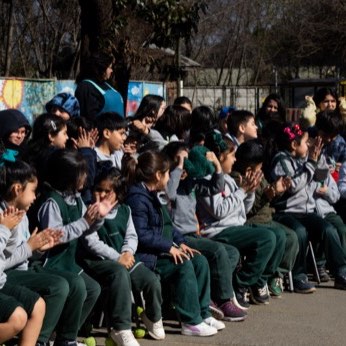 El patio lleno de escolares de uniforme verde, sentados en el suelo.