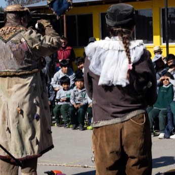 Un artista de abrigo largo camina por el centro del patio, rodeado de escolares.