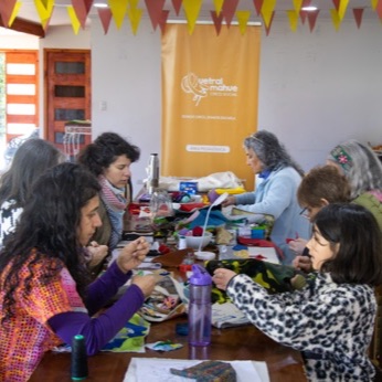 La sala del Colegio de Profesores con la mesa larga llena de participantes bordando, bajo los banderines del festival.