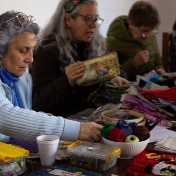 Varias mujeres bordan alrededor de la mesa; una de ellas sostiene en alto una arpillera terminada.