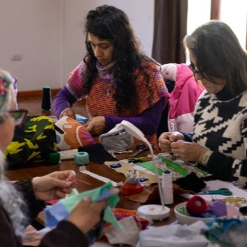 Tres participantes cosen retazos de tela, unas sentadas y otra de pie junto a la mesa.