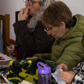 Dos participantes concentradas en su trabajo, con las telas y las tijeras sobre la mesa.