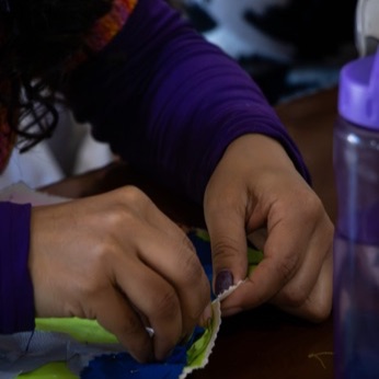 Primer plano de dos manos dando puntadas en el borde de una tela verde y azul.