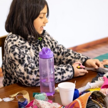 Una niña recorta telas en su puesto de la mesa.