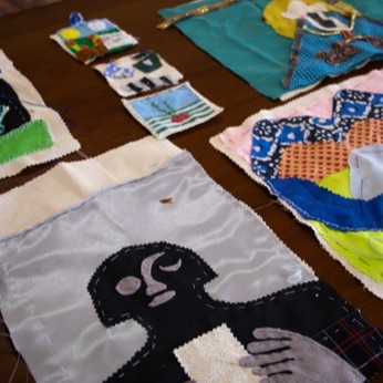 Varias arpilleras extendidas; en primer plano una figura oscura con las manos abiertas.