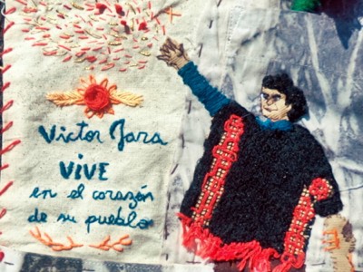 Arpillera bordada con la figura de Víctor Jara con el brazo en alto y la frase «Víctor Jara vive en el corazón de su pueblo».