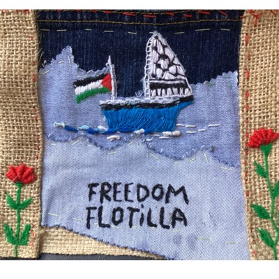 Arpillera sobre saco y mezclilla con un barco bordado, una bandera palestina y la frase «Freedom Flotilla», entre claveles rojos.