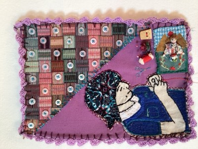 Arpillera de borde tejido lila con una mujer de delantal azul bordando, junto a un tejido de retazos con botones.