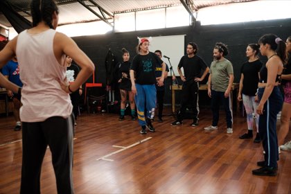 El profesor, con una gorra de orejas, muestra un movimiento en medio de la rueda de participantes.